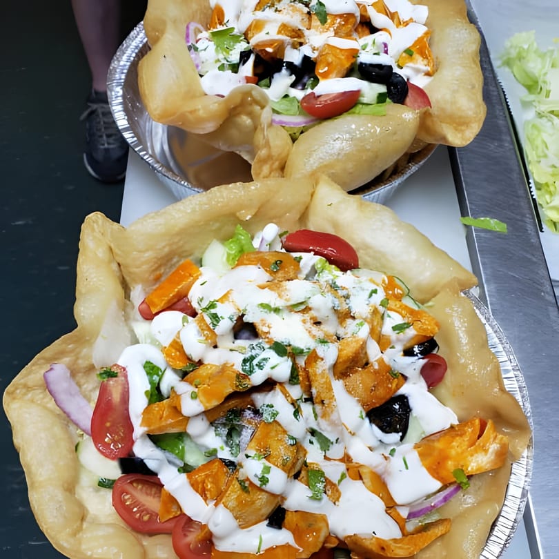 Two vibrant chicken taco salads in crispy tortilla bowls, topped with fresh vegetables and creamy dressing.