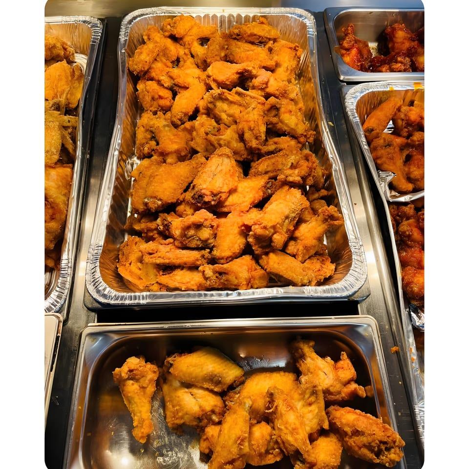Buffet trays filled with golden fried chicken pieces, including wings, drumsticks, and breaded chicken.