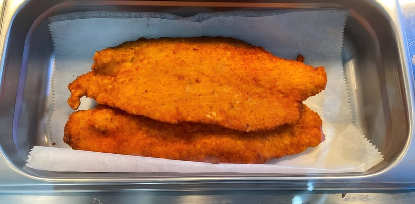Two crispy, golden-orange breaded cutlets in a metal serving tray.